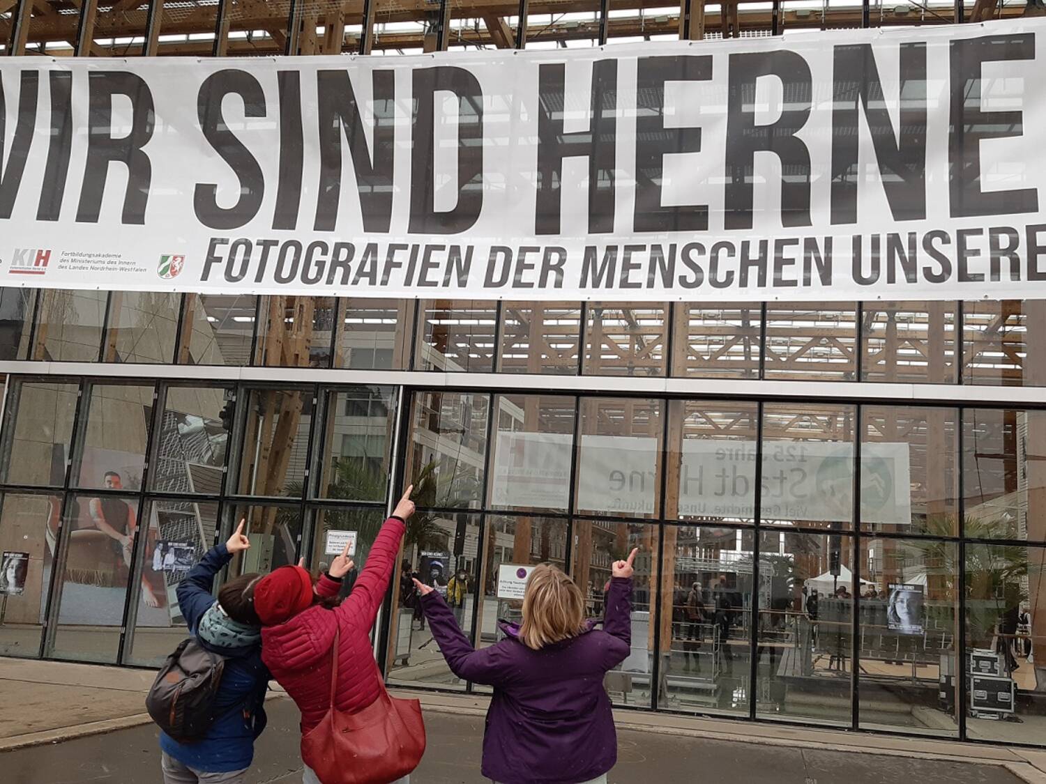 Drei Personen zeigen auf einen großen Banner WIR SIND HERNE