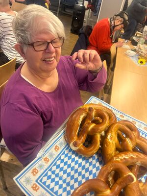 Eine Frau sitzt am Tisch und bekommt eine Brezel.