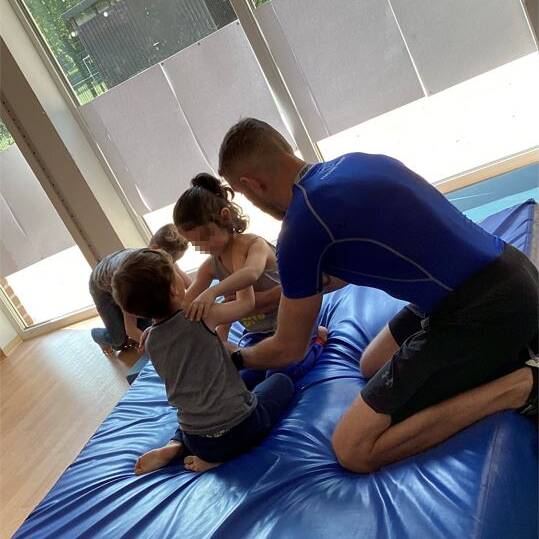 Zwei Kinder und ein Erwachsener befinden sich auf einer dicken blauen Matte