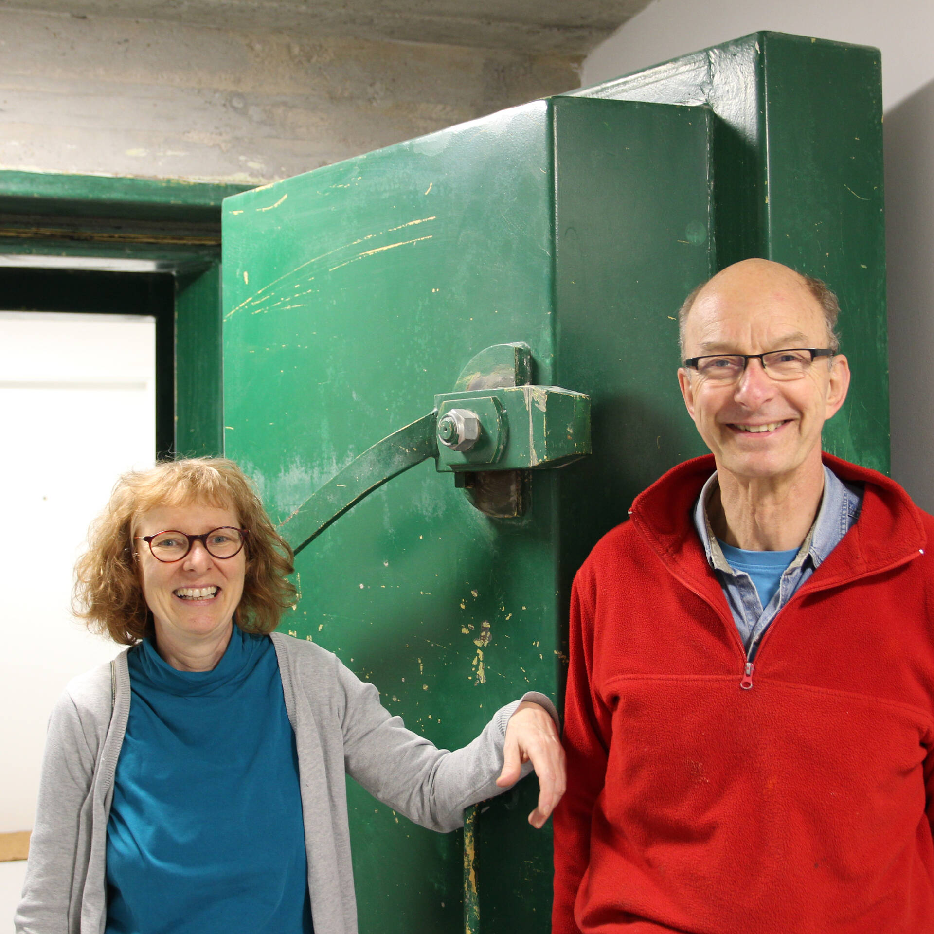 Eine Frau und ein Mann stehen vor einer dicken grünen Stahktüre