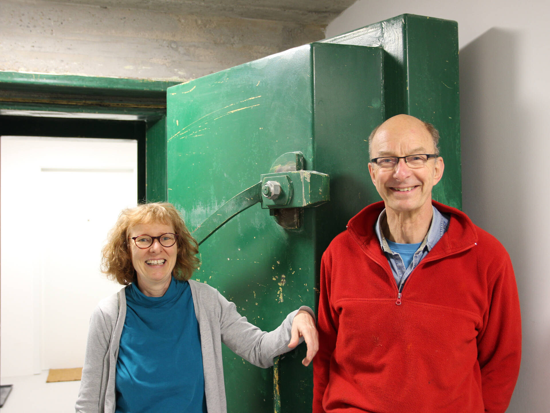 Eine Frau und ein Mann stehen vor einer dicken grünen Stahktüre