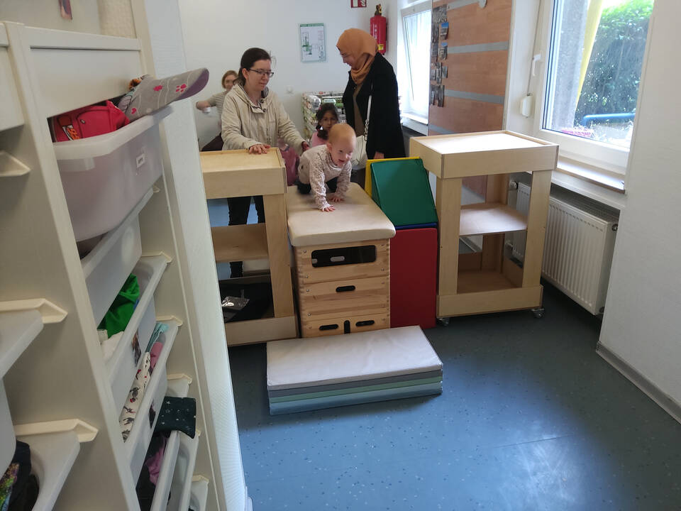 Ein Kind krabbelt über einen Bock und zwei Frauen stehen daneben.