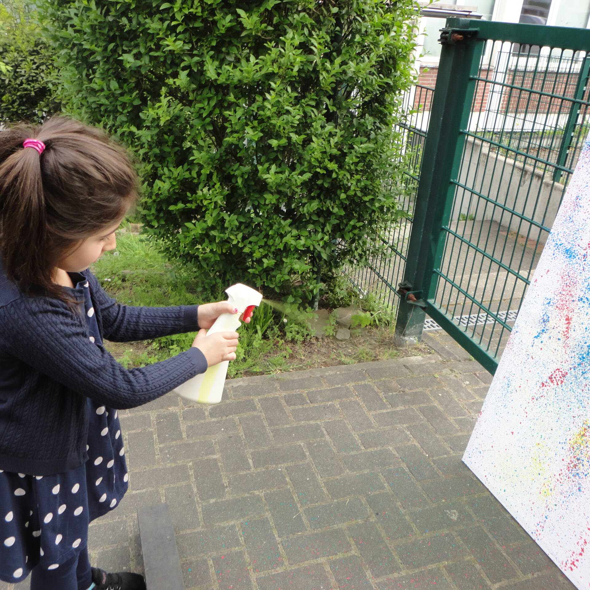 Ein Mädchen spritzt mit Frabe auf eine weiße Fläche