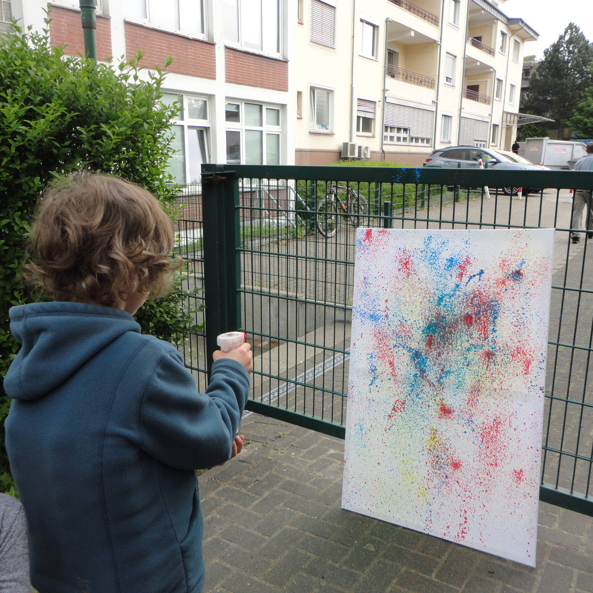 Ein Kind spritzt mit Frabe auf eine weiße Fläche