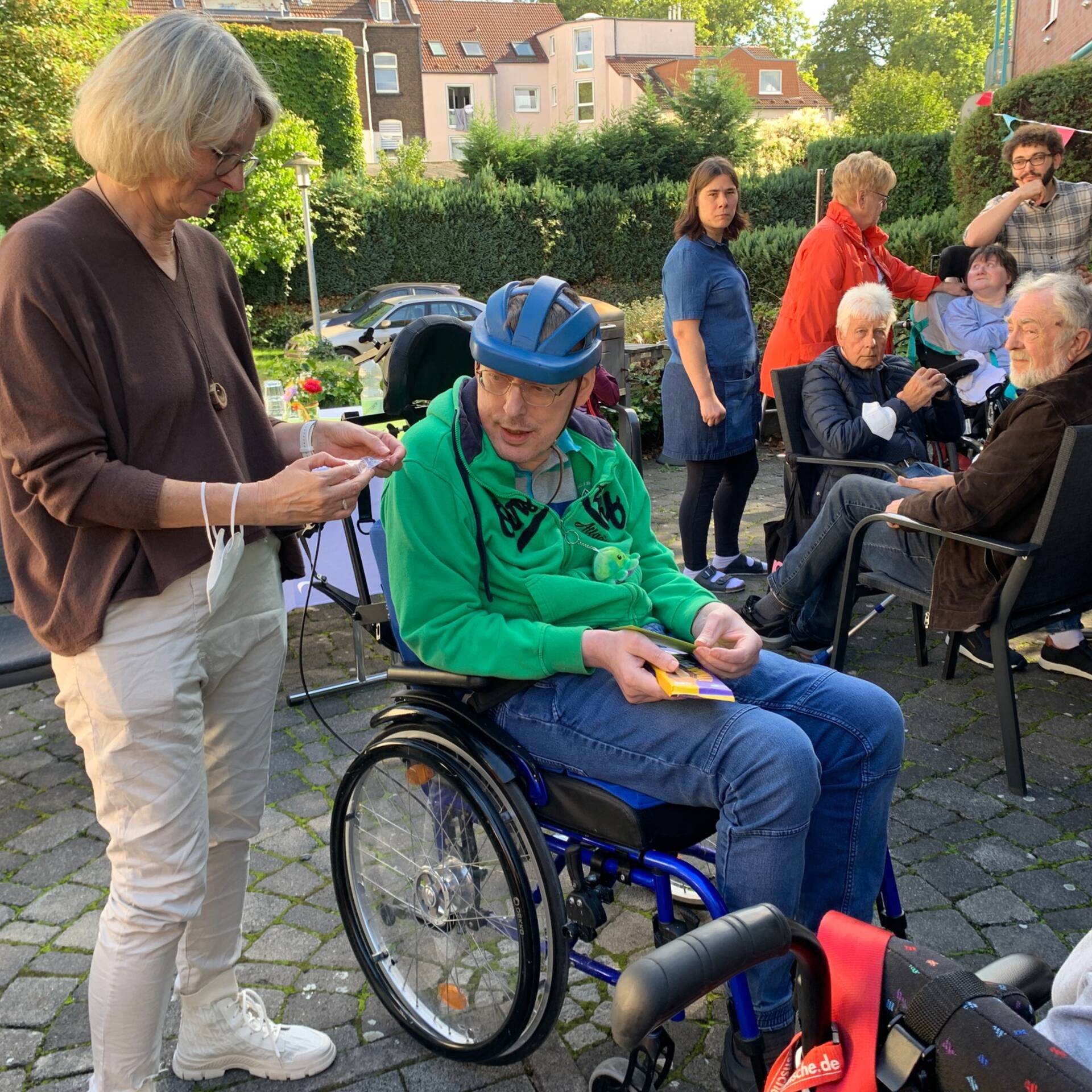 Mehrere Personen die draussen sitzen, zum Teil in Hilfsmitteln.