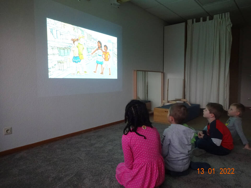 Vier Kinder schauen etwas auf einer Leinwand und sitzen auf dem Boden.