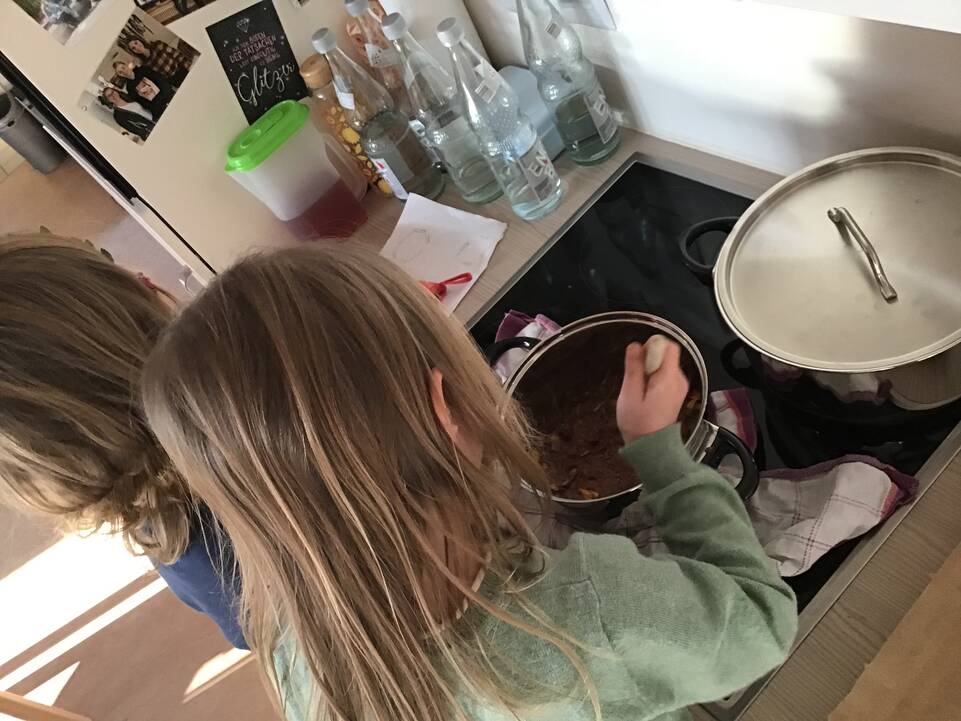 Zwei Kinder verrühren Schokolade im Kochtopf.