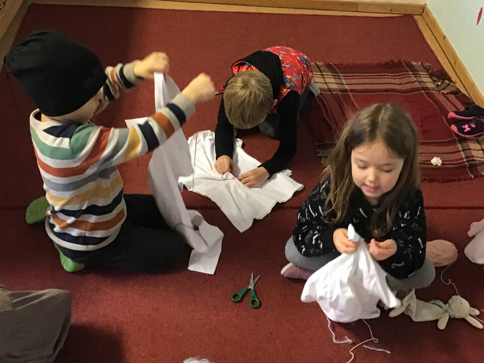 Drei Kinder sitzen auf dem Boden und haben Stoffe und Wolle ind der Hand.