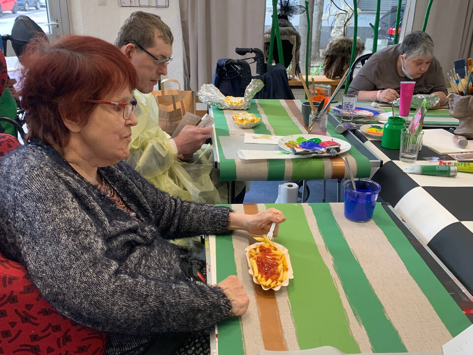 Mehrere Menschen an einem Tisch die mit Farbe arbeiten.