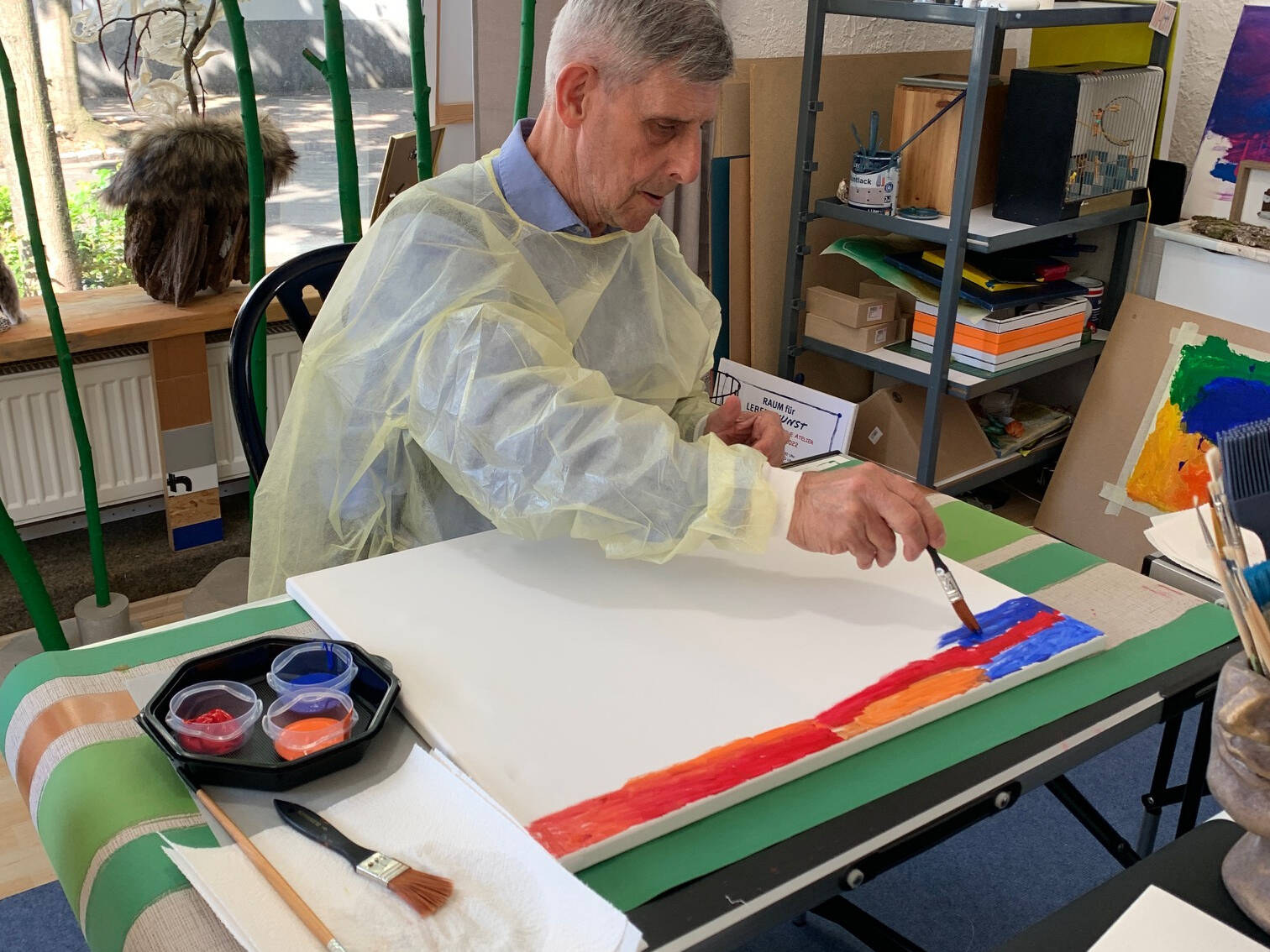 Ein Mann malt bunbte Streifen auf einen weißen Untergrund.