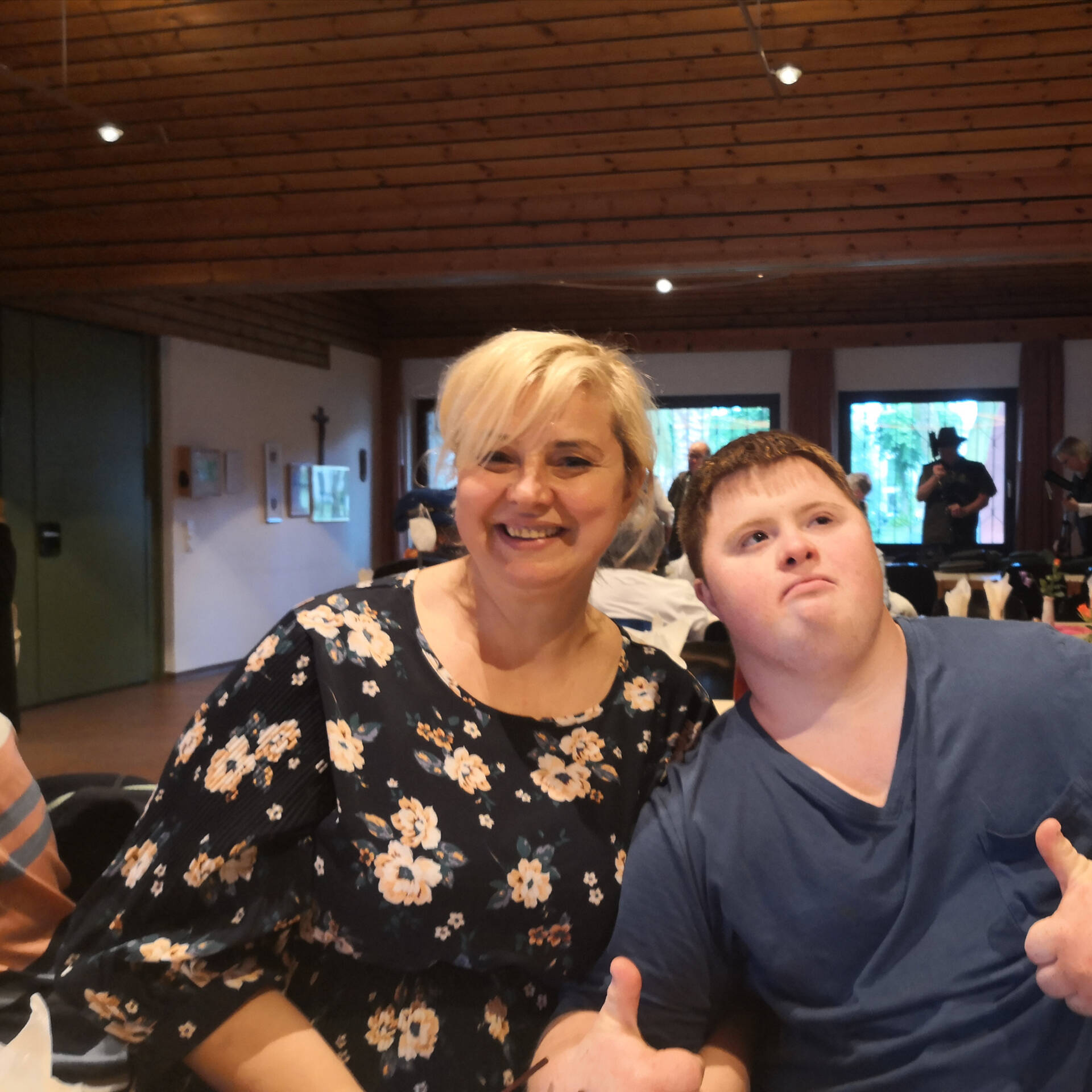 Eine Frau sitzt neben einem Mann im Raum, der Mann zeigt mit den Daumen hoch.