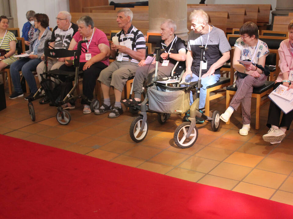 Mehrere Menschen sitzen in der Kirche und haben zum Teil Hilfsmittel dabei. 