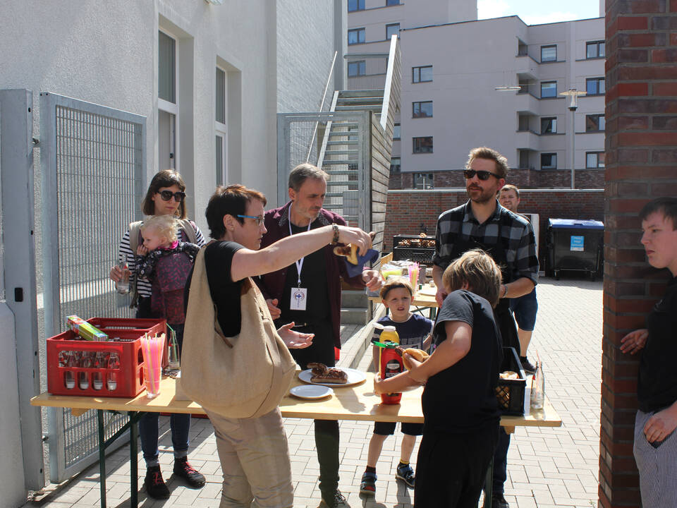 Mehrere Menschen stehen draußen auf einem Tisch liegen unterschiedliche Dinge.