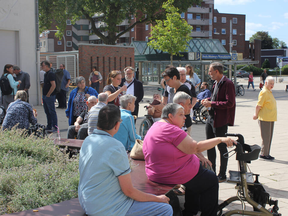 Viele Menschen stehen oder sitzen auf einem Platz.