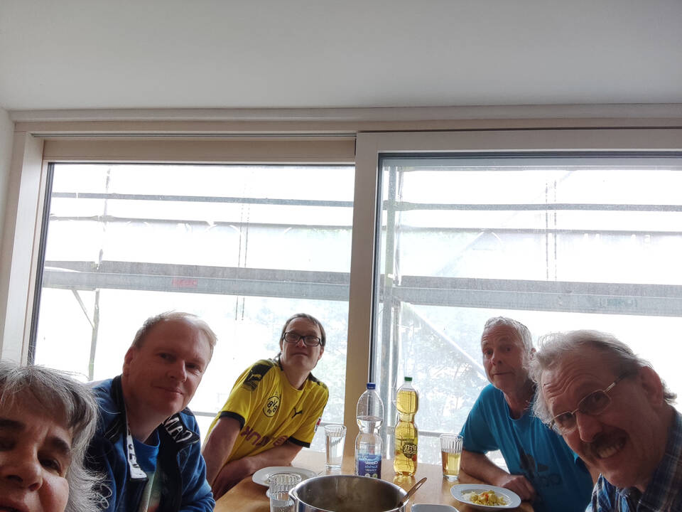 Fünf Peronen sitzen an einem Tisch, darauf steht ein Topf und Teller mit Essen.