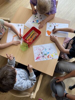 Kinder sitzen am Tisch und malen bunte Bilder.