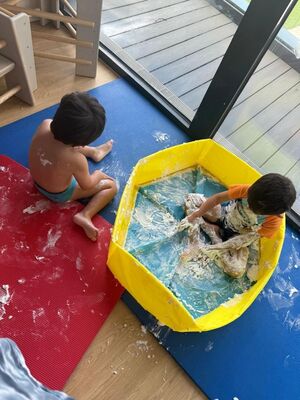 Kinder sitzen auf dem Boden auf Matten und spielen mit Schaum.
