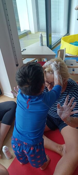 Ein Kind mit eingeschäumten Händen streicht einer Person über die Haare.