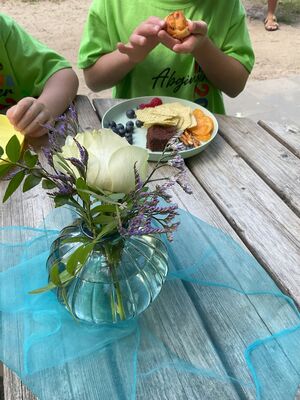 Es stehen Blumen auf dem Tisch und man sieht einen Teller mit vielen Leckereien.