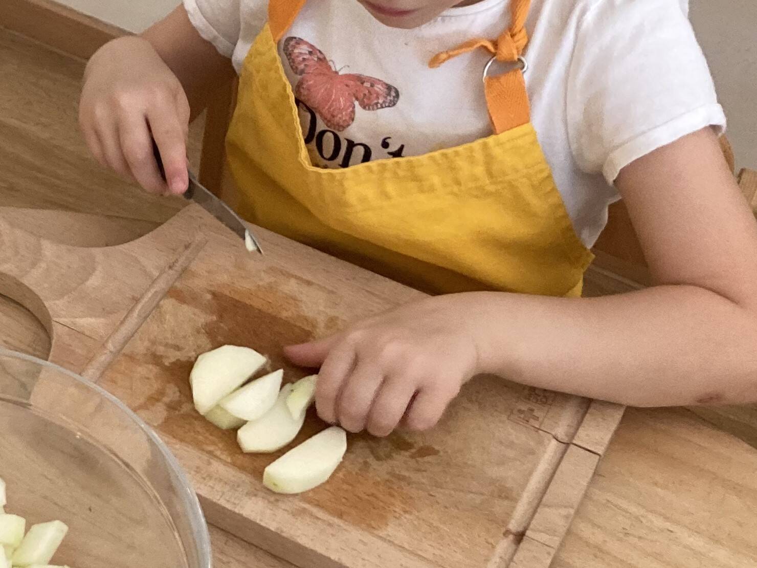 Apfelspalten auf eine Holzbreitt, Kinderhände in einer ein Messer.