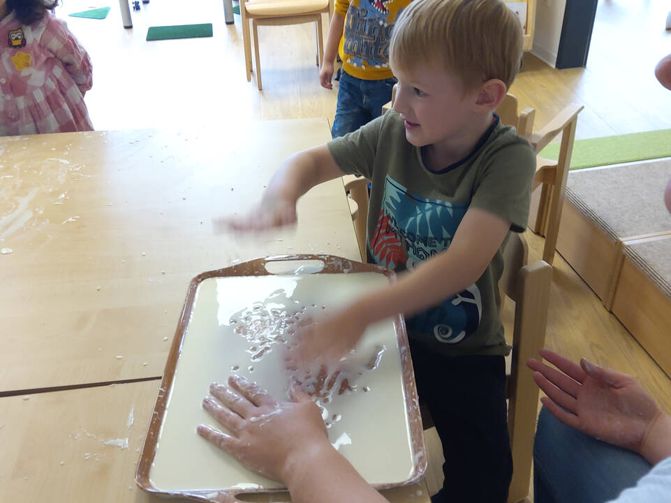 Mehrere Kinder sitzen am Tisch und Mischen Wasser und Speisestärke mit den Händen.