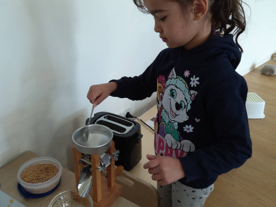 Ein Kind füllt Körner in die Kornquetsche.