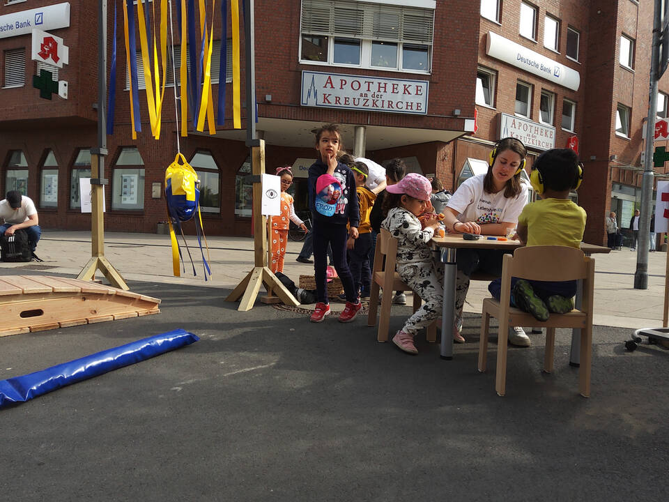 Kinder sitzen an einem Tisch mit einer Frau, draussen.