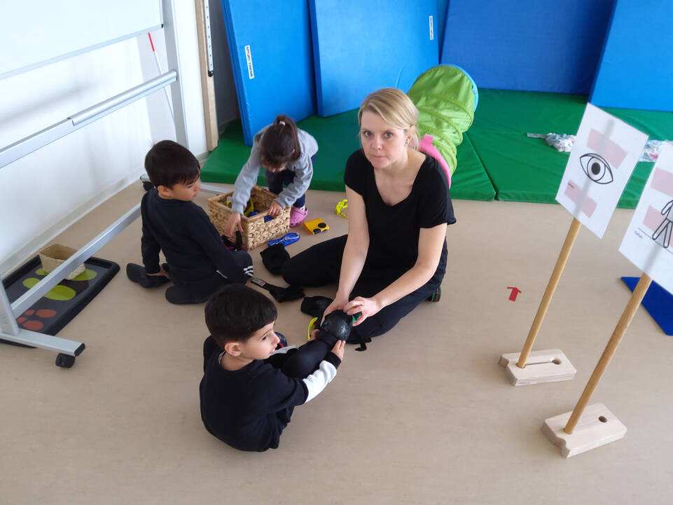 Kinder sitzen mit einer Frau auf dem Boden. 