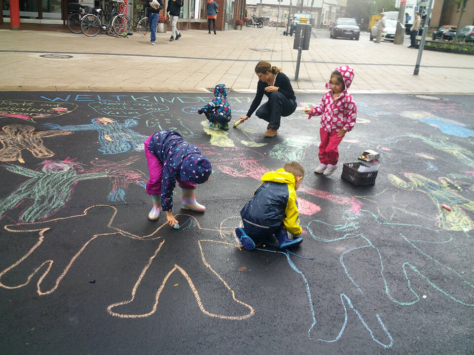 Kinder malen mit Kreide Menschen auf eine Straße.