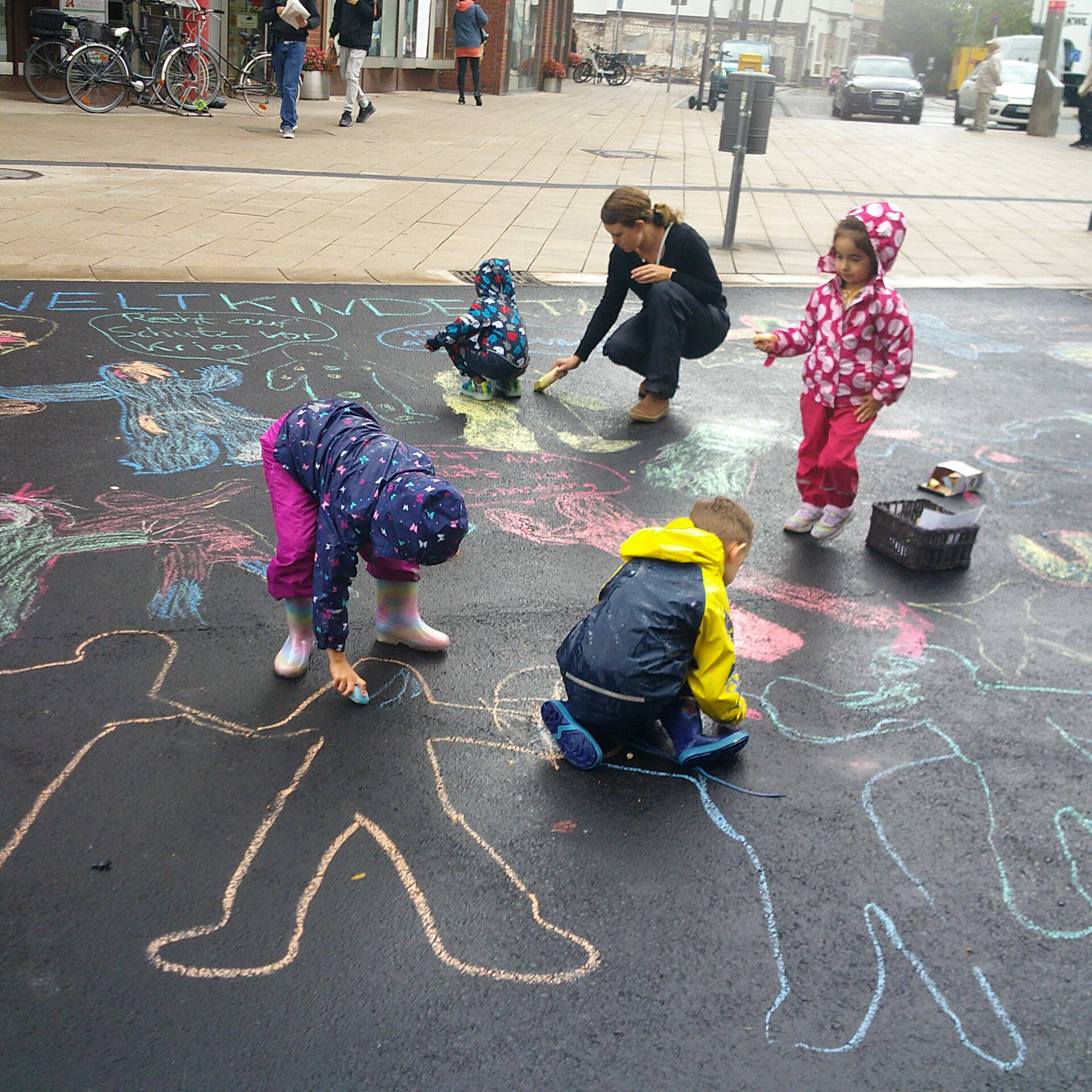 Kinder malen mit Kreide Menschen auf eine Straße.