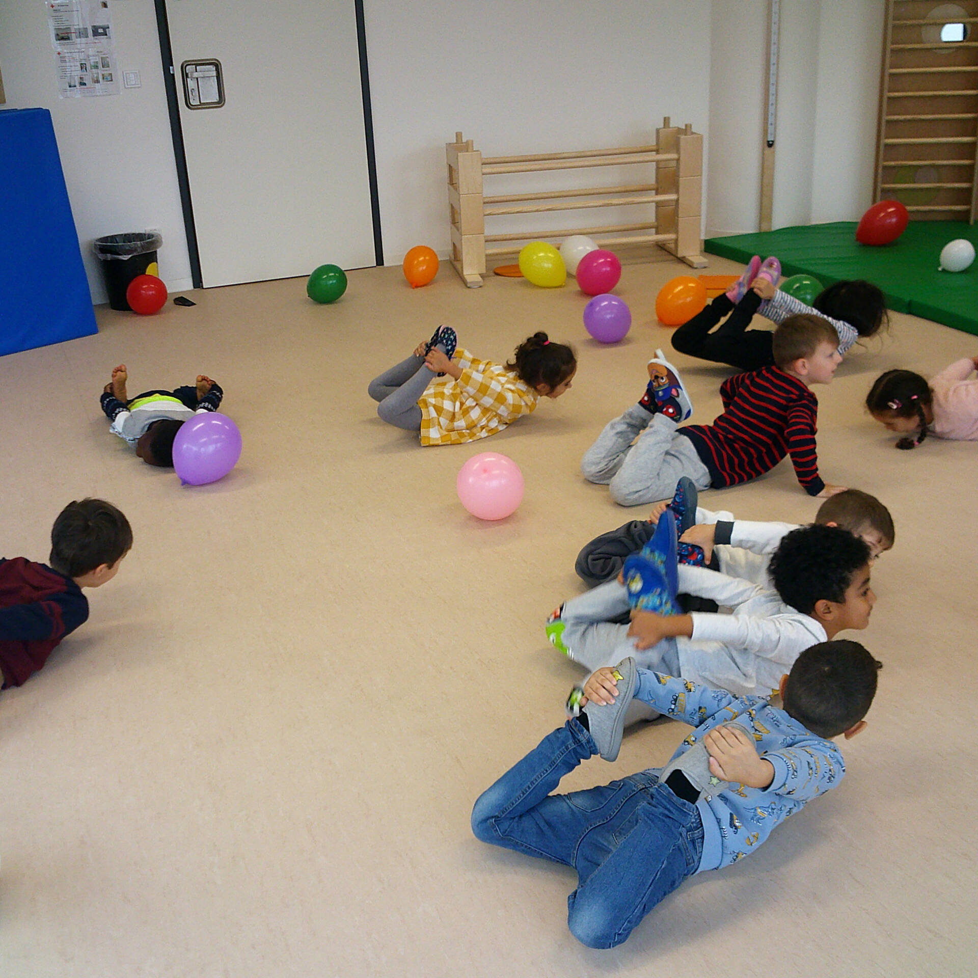 Kinder liegen auf dem Bauch und halten ihre Beine mit den Händen nach oben.