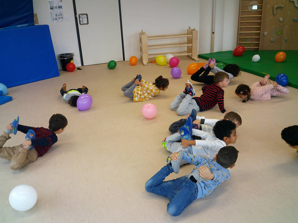 Kinder liegen auf dem Bauch und halten ihre Beine mit den Händen nach oben.