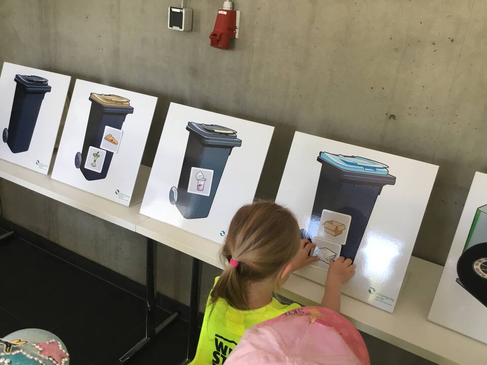Ein Mädchen klebt etwas auf eine abgebildete Mülltonne.