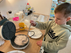 Ein Kind gibt Waffelteig in ein Waffeleisen.