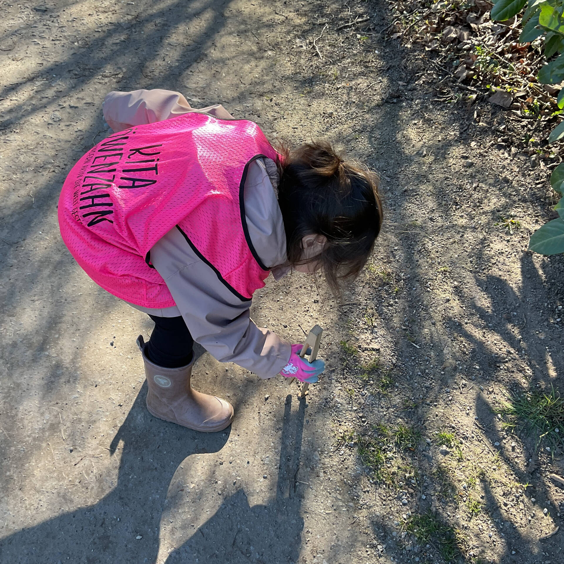 Ein Kind mit einer Weste hebt etwas auf.