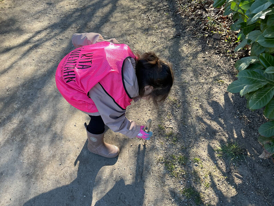 Ein Kind mit einer Weste hebt etwas auf.