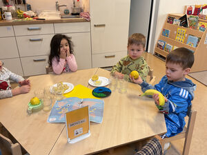 Kinder sitzen an einem Tisch und haben zum Teil Obst in der Hand.