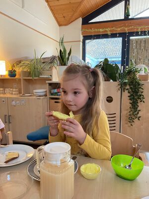 Ein Mädchen sitzt an einem Tisch und hat ein Brot in der Hand.