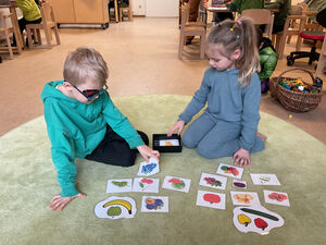 Kinder sitzen auf dem Boden und schauen sich Karten mit Obst und Gemüse an.