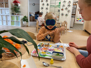Ein Kind probiert mit verbundenen Augen insbesondere orange Lebensmittel