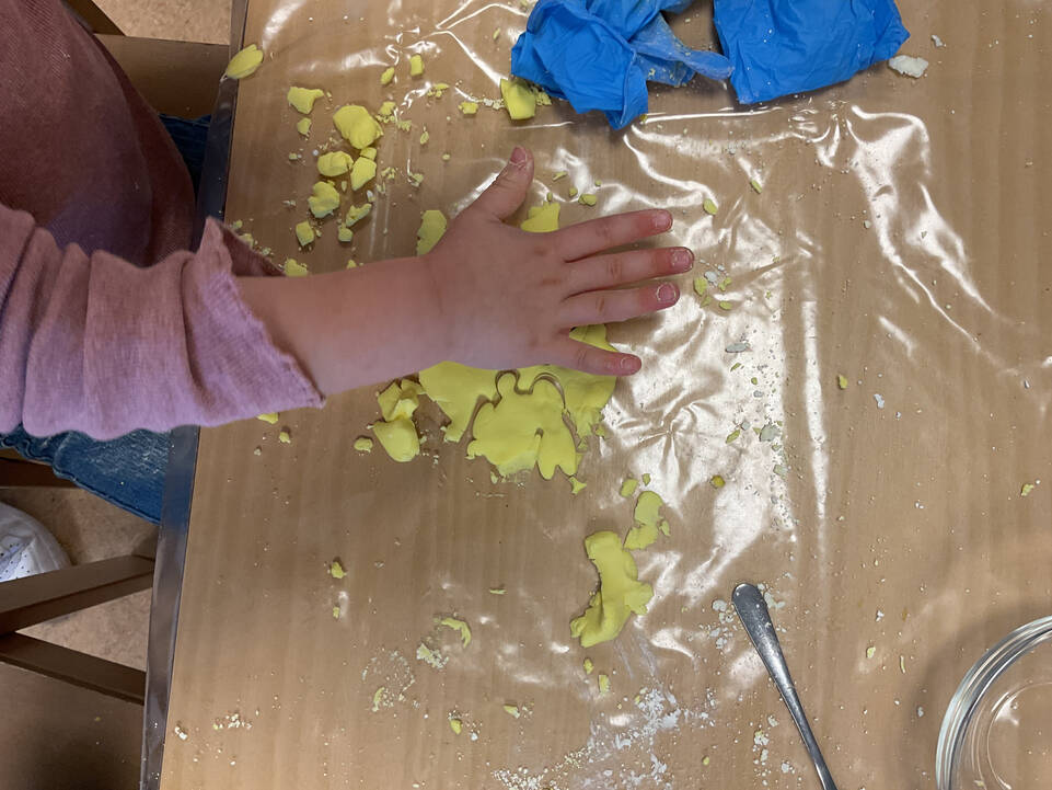 Eine Kinderhand auf einer gelben Masse.