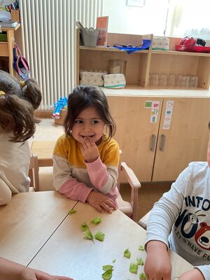 Kinder sitzen am Tisch und probieren Erbsen