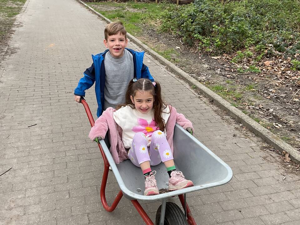 Ein Junge schieb ein Mädchen, welches in der Schubkarre sitzt.