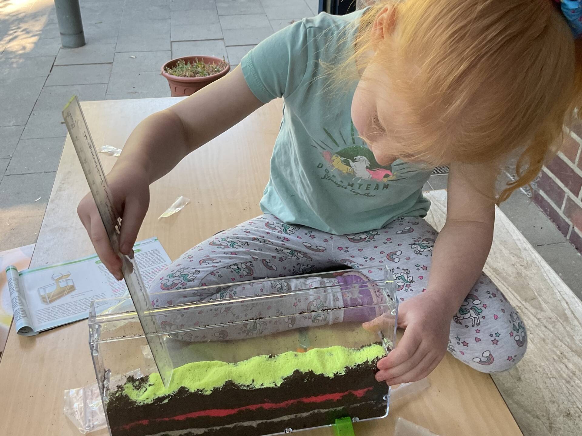 Ein Kind misst die Höhe eines schmalen Schaugefäßes.