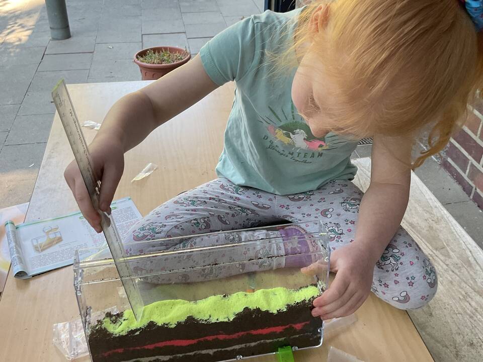 Ein Kind misst die Höhe eines schmalen Schaugefäßes.