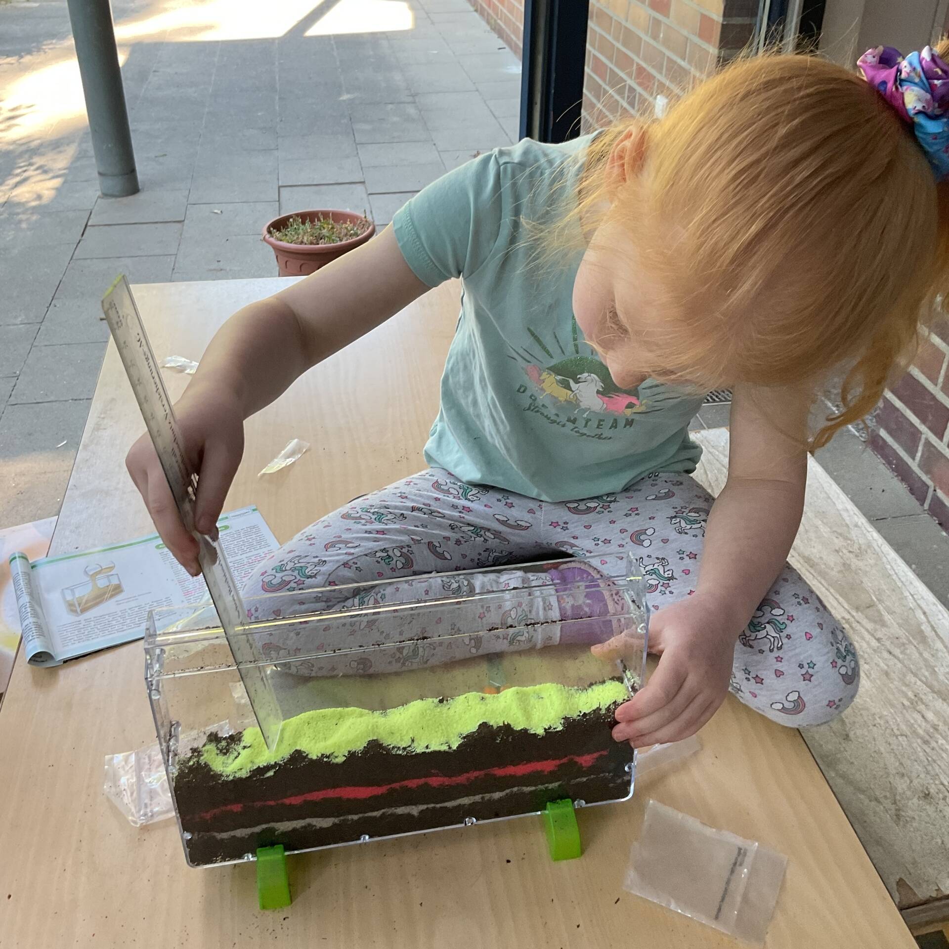 Ein Kind misst die Höhe eines schmalen Schaugefäßes.