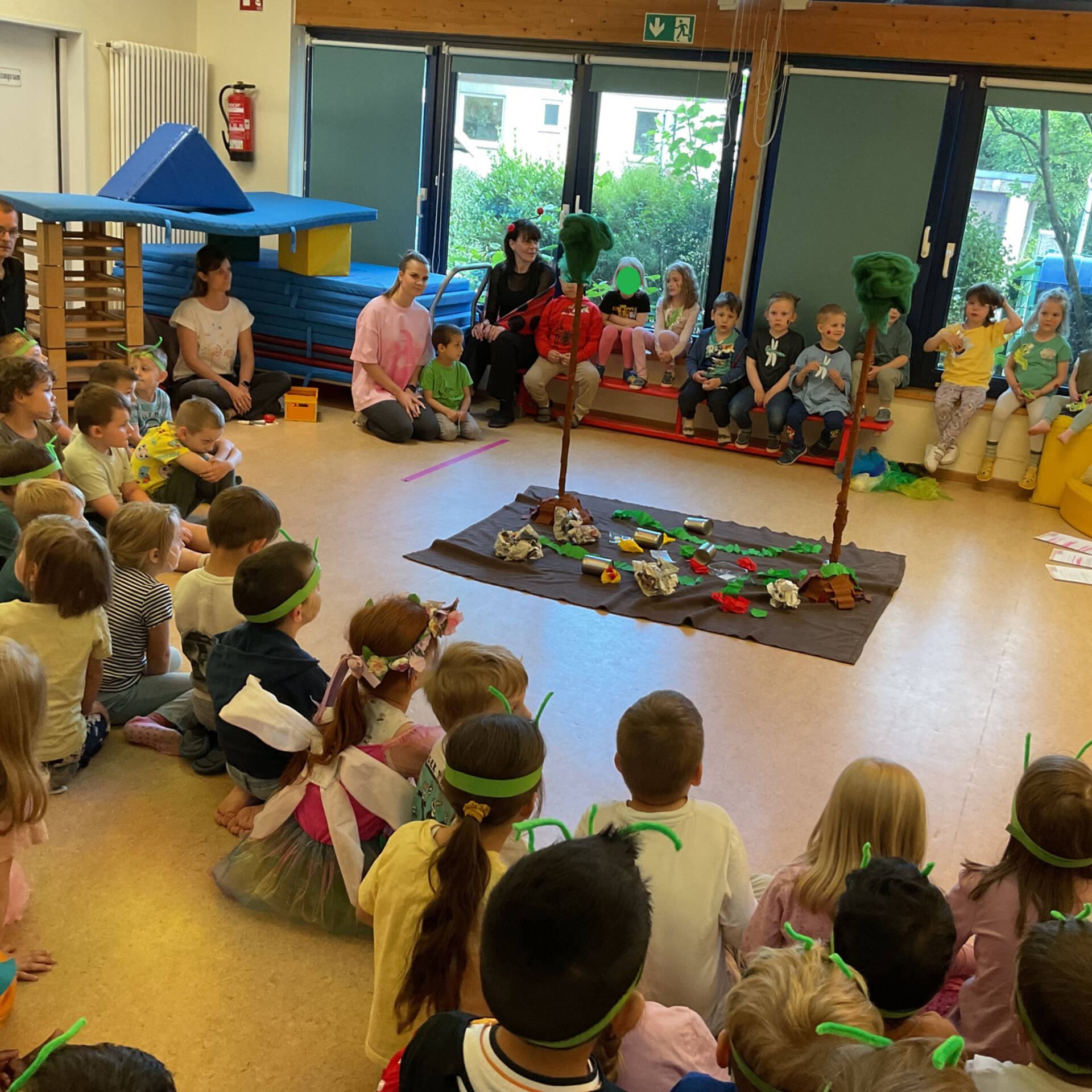 Viele Kinder sitzen im Kreiss in einem Raum, um ein Schaubild herum.