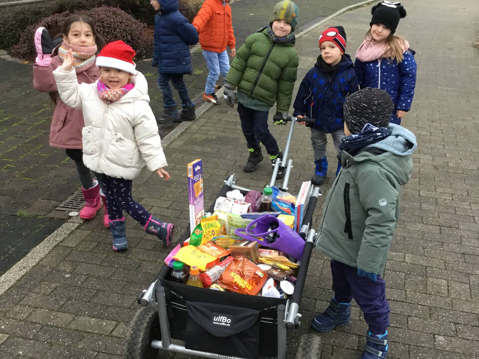 Viele Kinder mit Bollerwagen worin viele Lebensmittel sind.