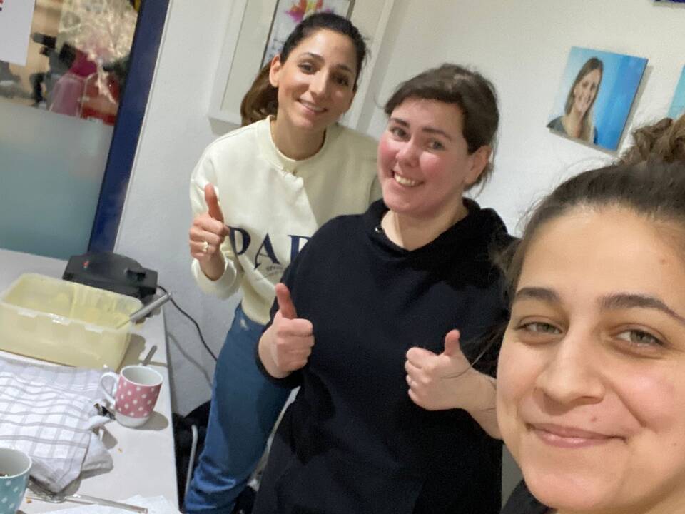 Drei Frauen hinter einem Tisch, sie lachen.