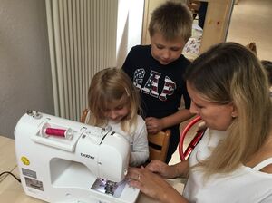 Zwei Kinder mit einer Frau an einer Nähmaschine